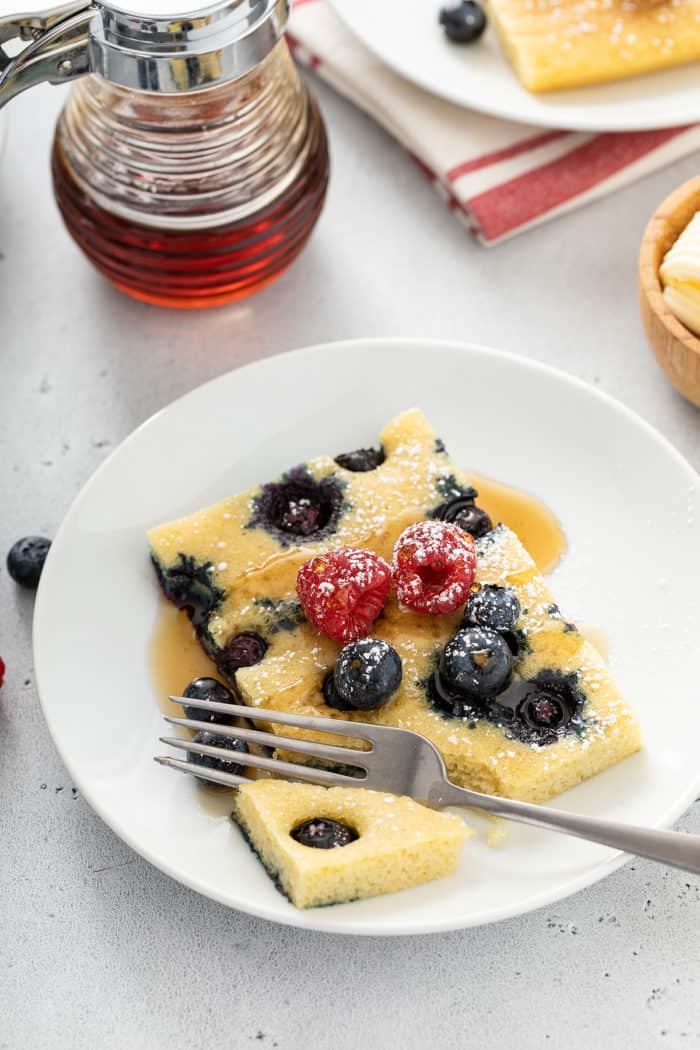 Fork taking a bite of a blueberry sheet pan pancake on a white plate