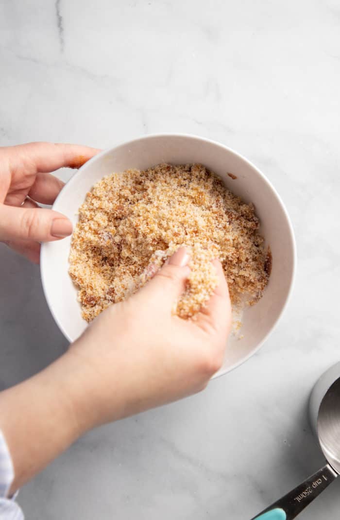 Hand rubbing together molasses and sugar in a white bowl