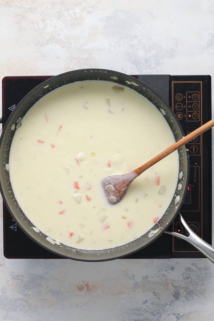 Sauce for chicken pot pie casserole being stirred with a wooden spoon in a skillet