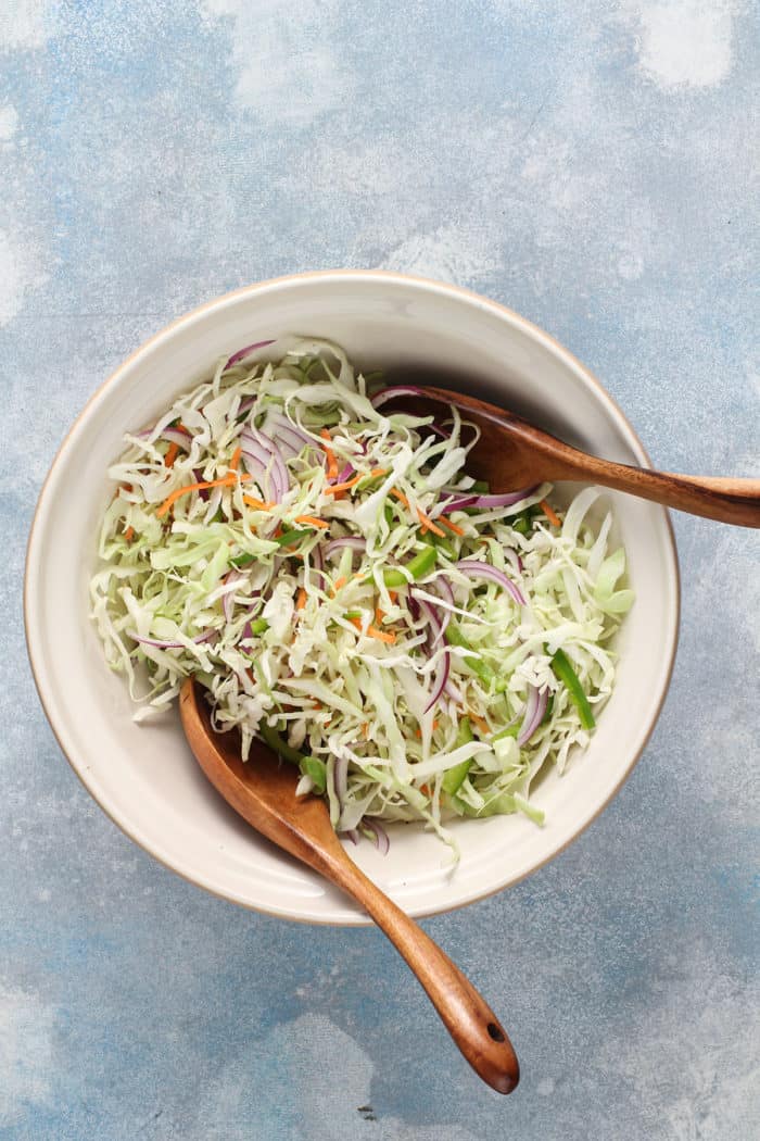 Sliced vegetables for coleslaw tossed together in a white mixing bowl