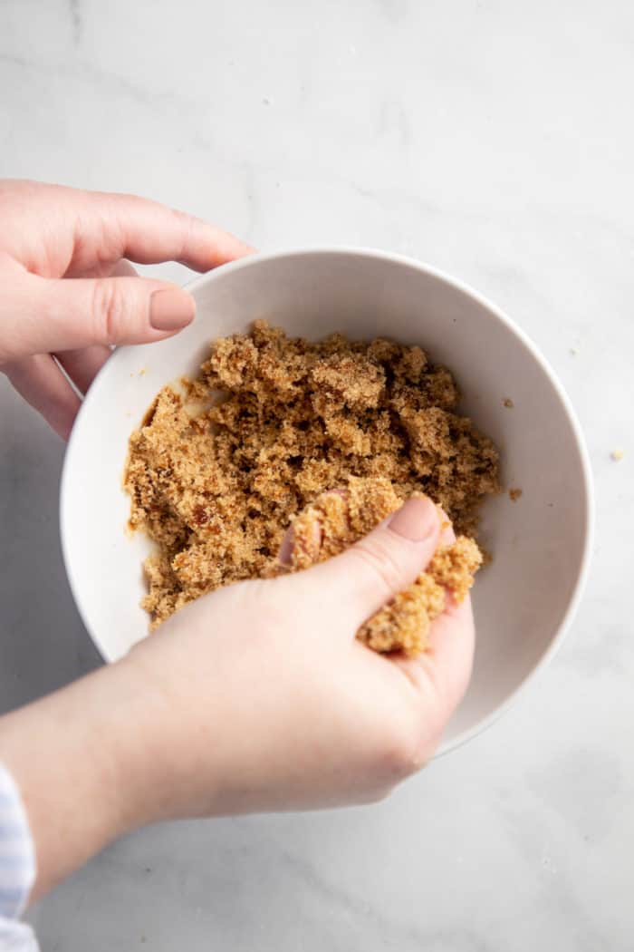 Hand rubbing together molasses and light brown sugar in a white bowl