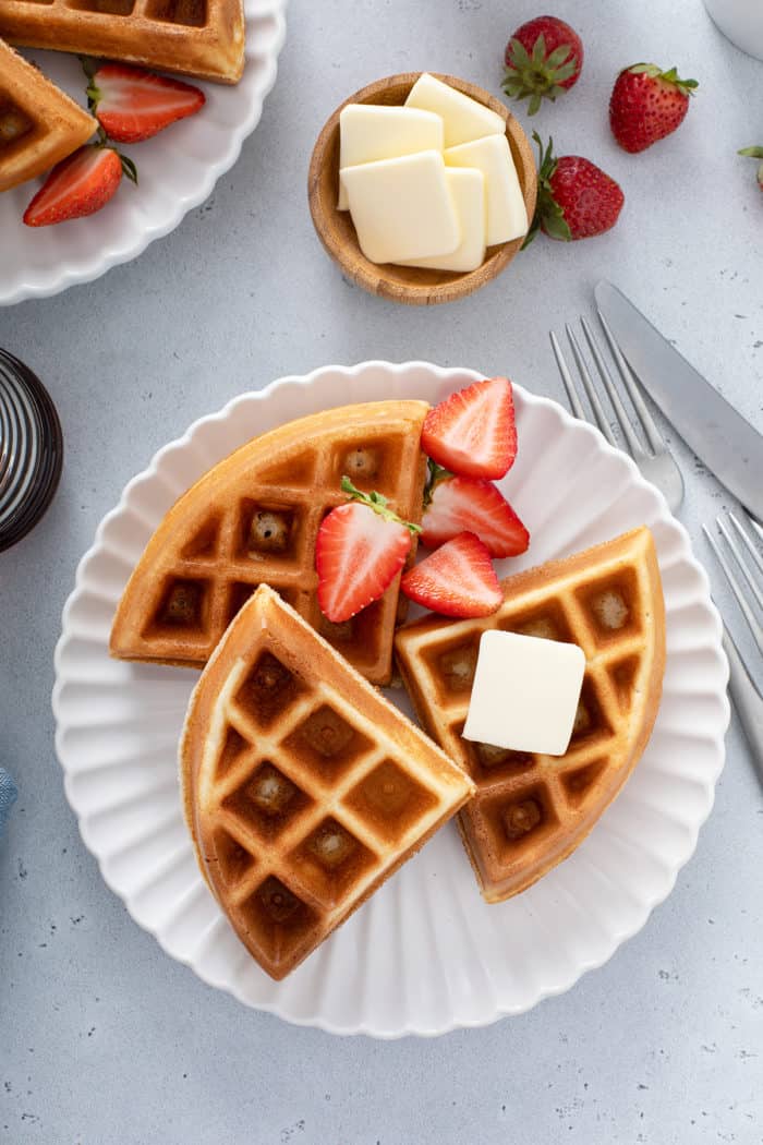 Overhead view of bisquick waffles on a white plate, topped with butter, syrup, and fresh strawberries