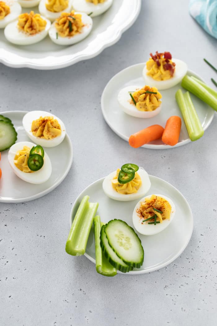 Three small white plates containing assorted cut veggies and deviled eggs