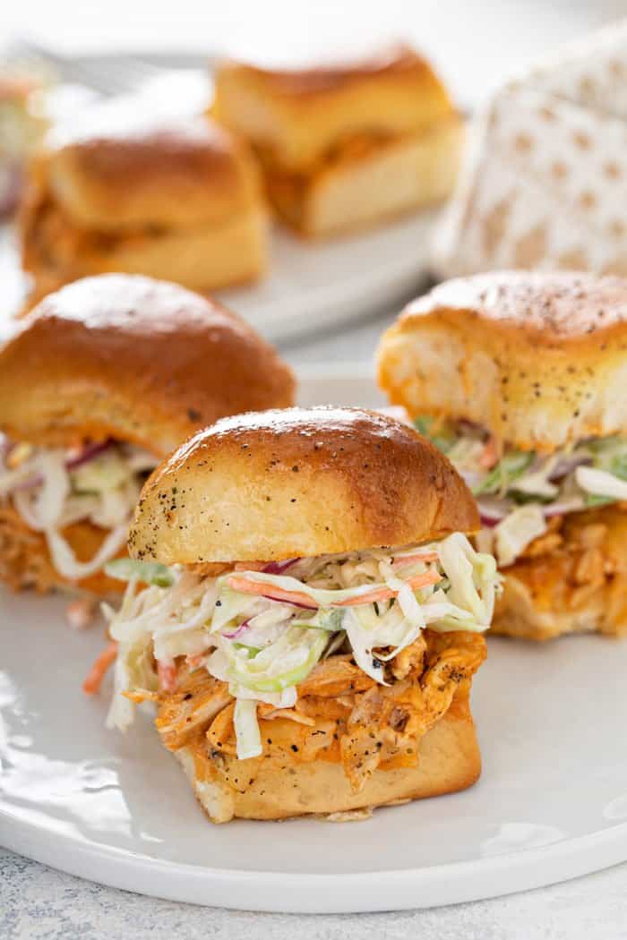 Buffalo chicken sliders topped with coleslaw on a white plate