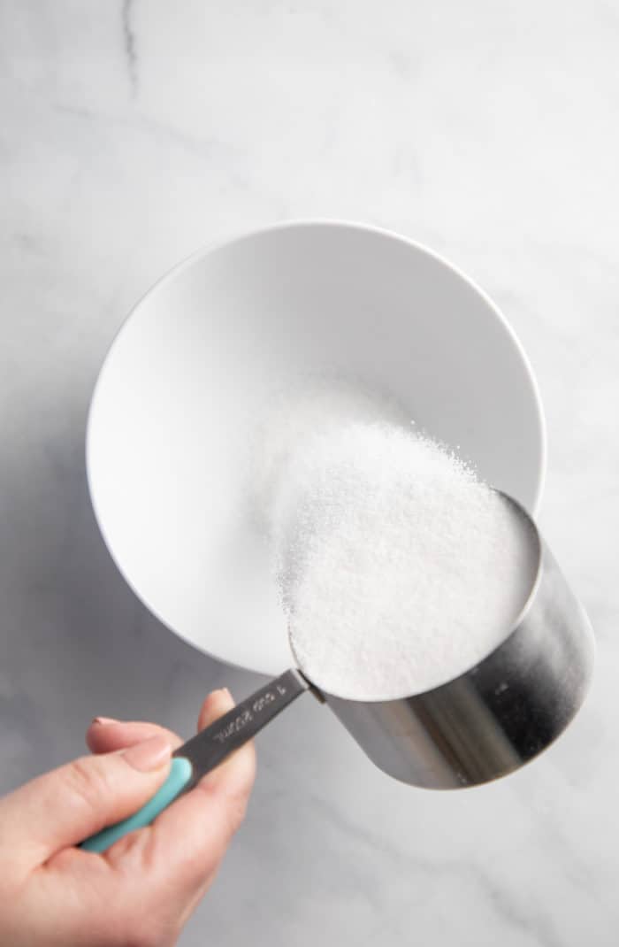 Granulated sugar being poured into a white bowl