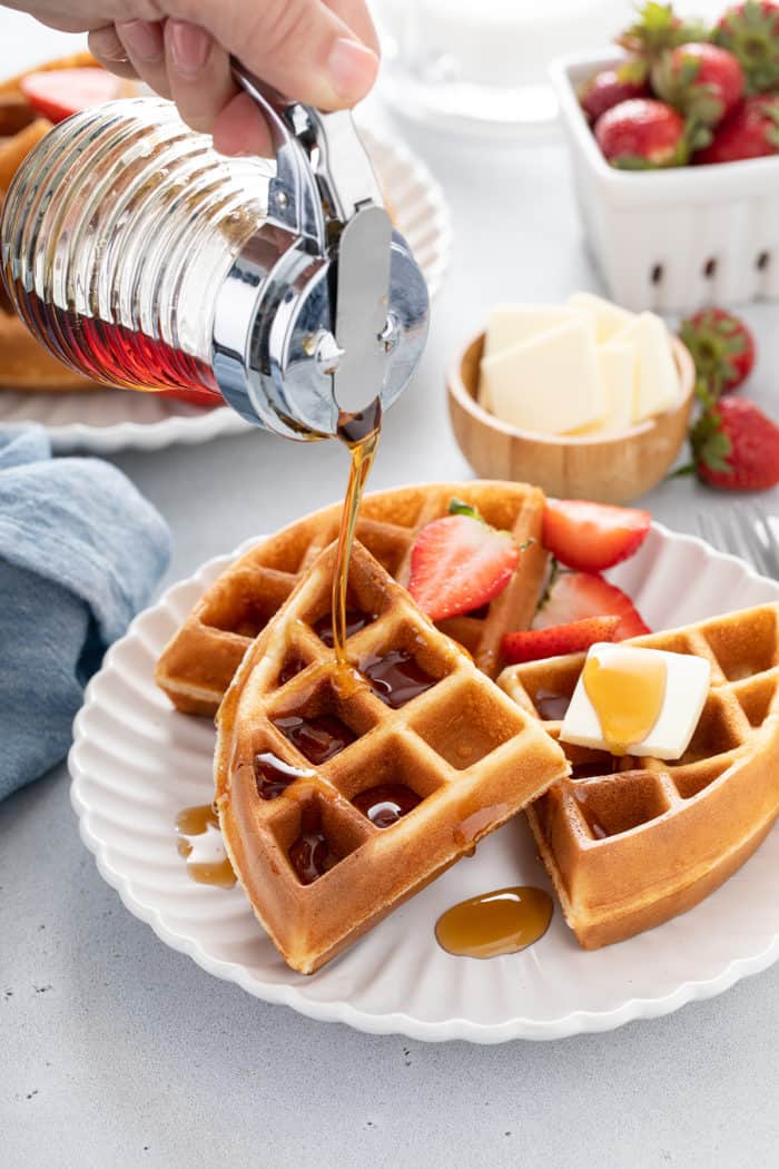 Syrup being poured over bisquick waffles on a white plate