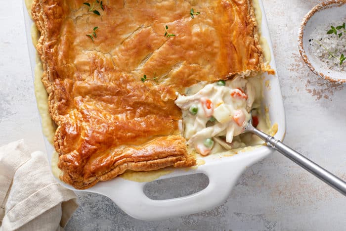 Spoon dishing out a serving of chicken pot pie casserole from a white baking dish