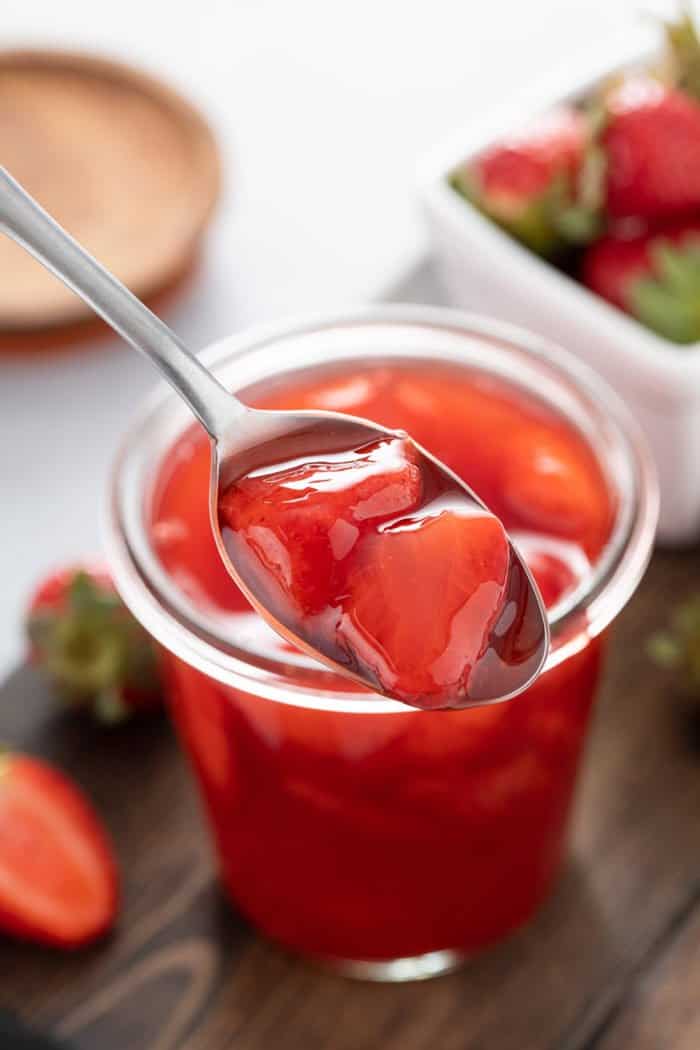 Spoon holding up a spoonful of homemade strawberry sauce in front of a jar of sauce