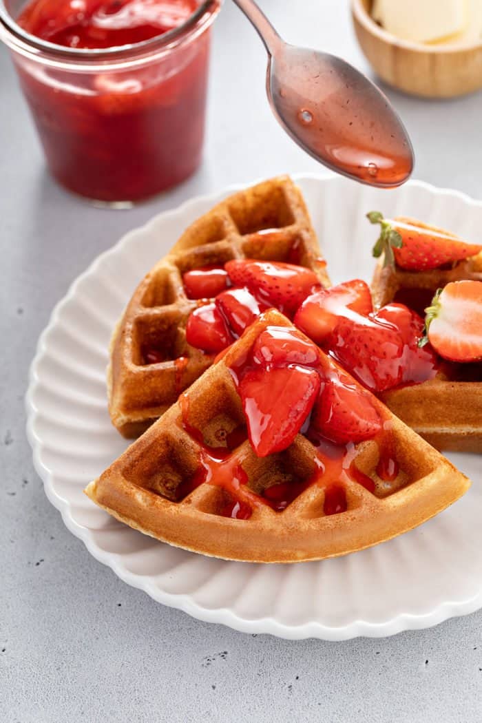 Strawberry sauce being spooned over the top of waffles