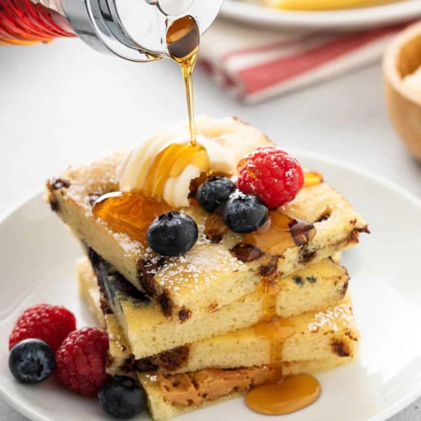 Syrup being poured over a stack of sheet pan pancakes on a white plate