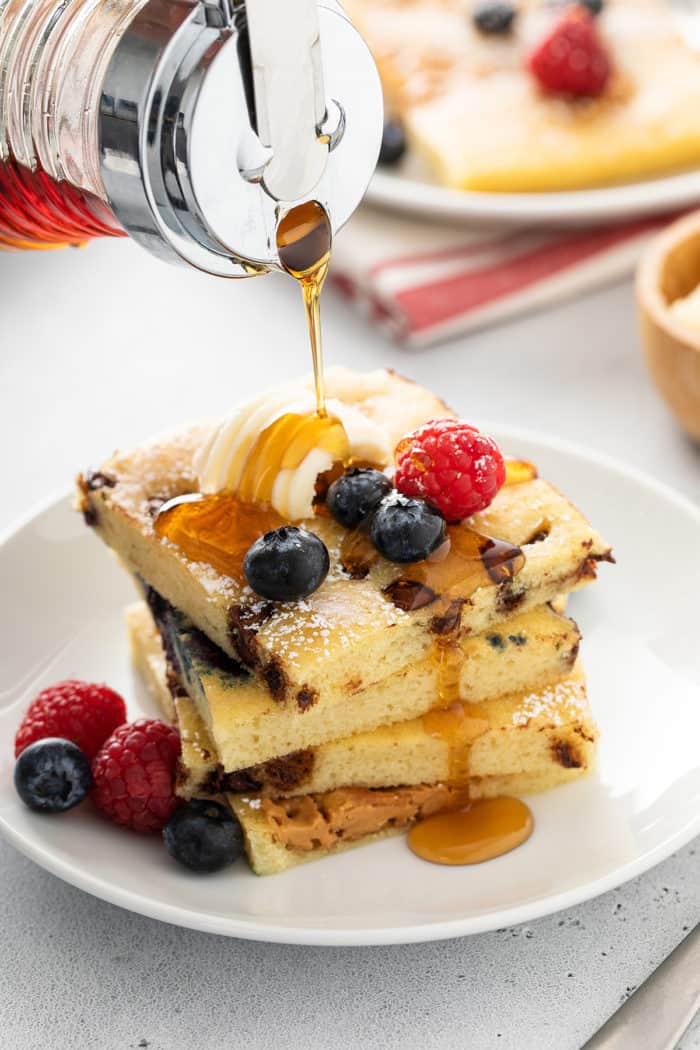 Syrup being poured over a stack of sheet pan pancakes on a white plate