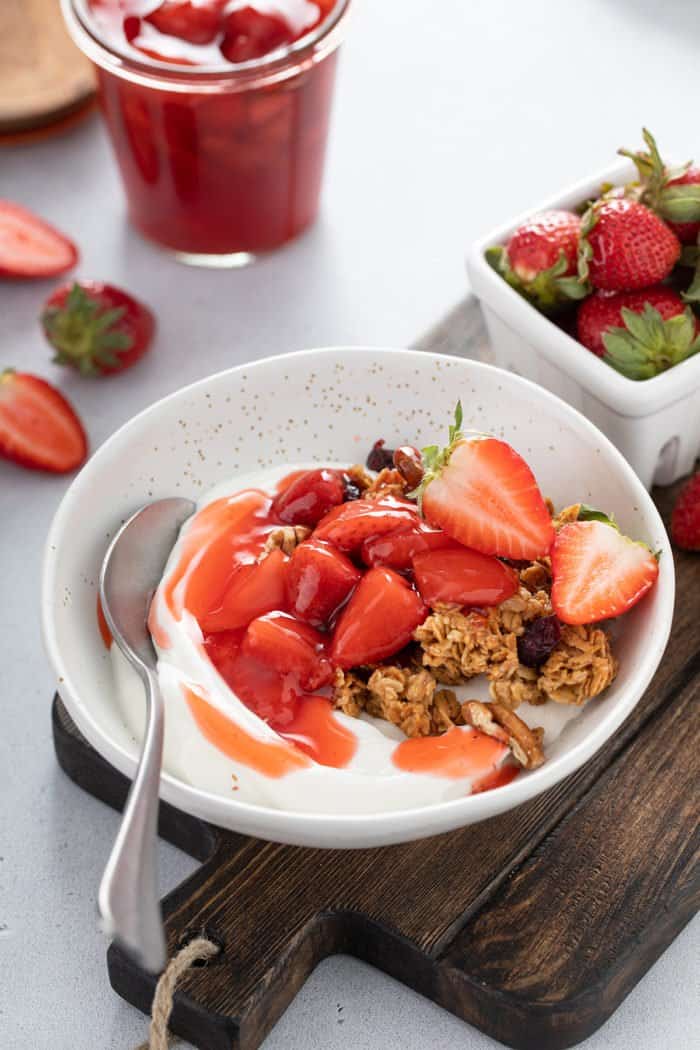 Strawberry sauce over yogurt and granola in a light-colored bowl