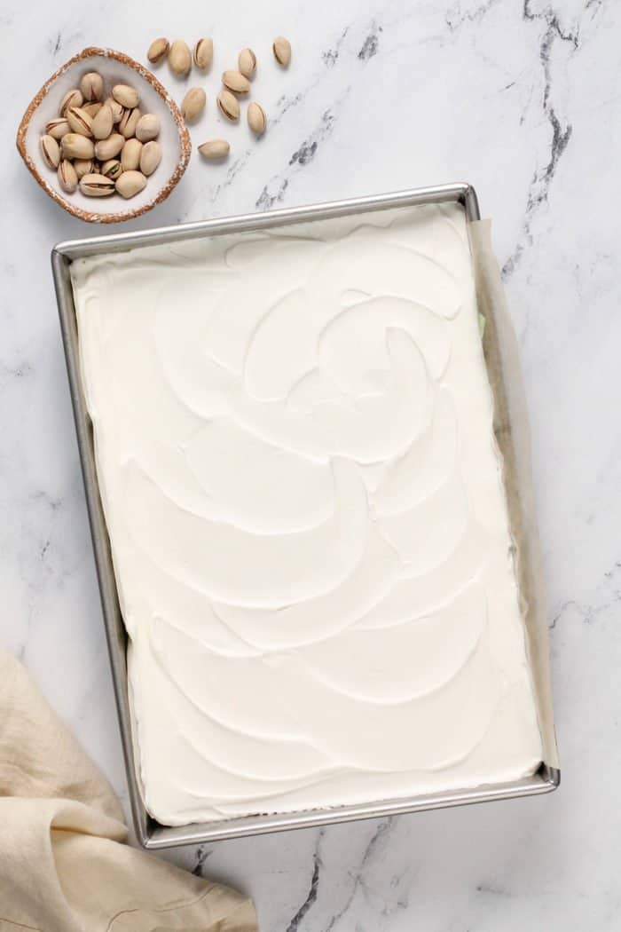 Assembled pistachio pudding dessert in a metal pan, ready to be chilled.