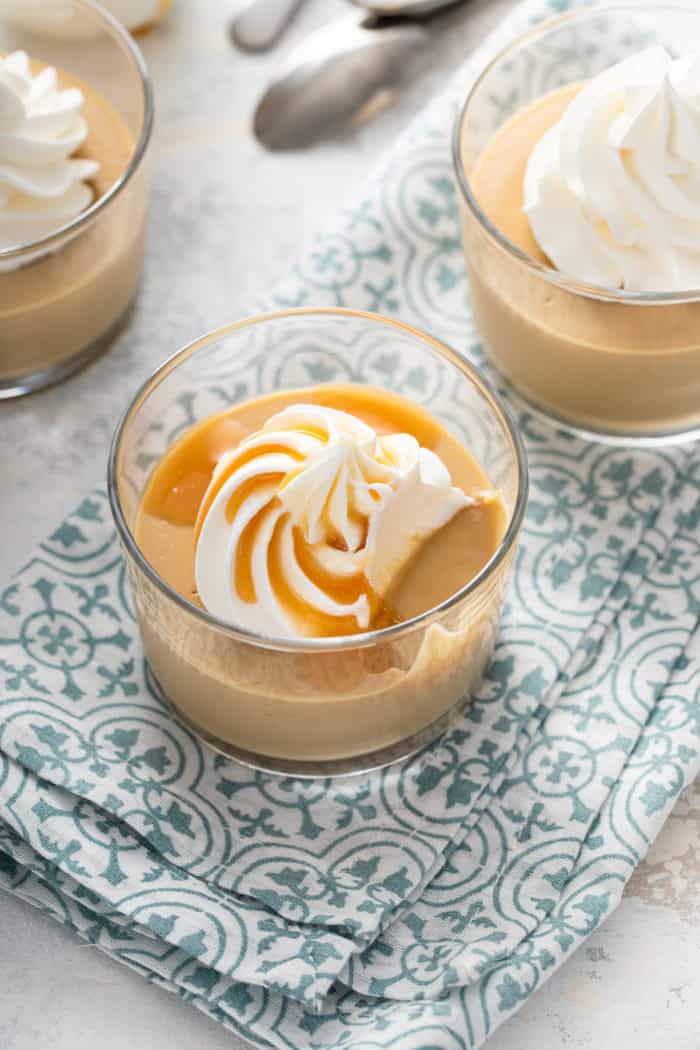 Small glass dish of butterscotch pudding topped with whipped cream and caramel sauce with a bite taken out of it.