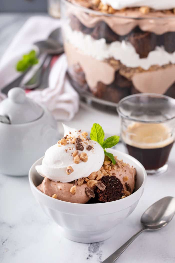 Small white bowl filled with brownie trifle set in front of a trifle dish.