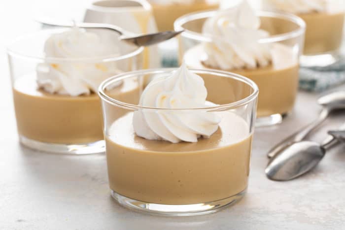 Close up of a glass bowl filled with butterscotch pudding, topped with a dollop of whipped cream.