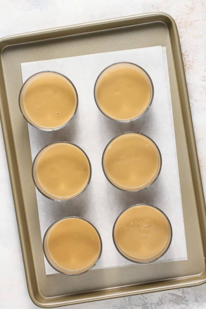 6 small dishes filled with butterscotch pudding, set on a sheet tray.