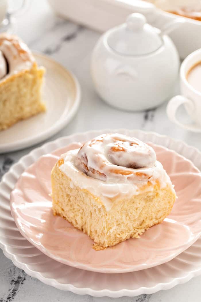 Close up of an iced cinnamon roll on a light pink plate