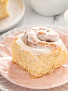 Close up of an iced overnight cinnamon roll set on a light pink plate