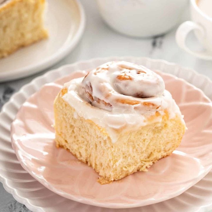 Close up of an iced overnight cinnamon roll set on a light pink plate