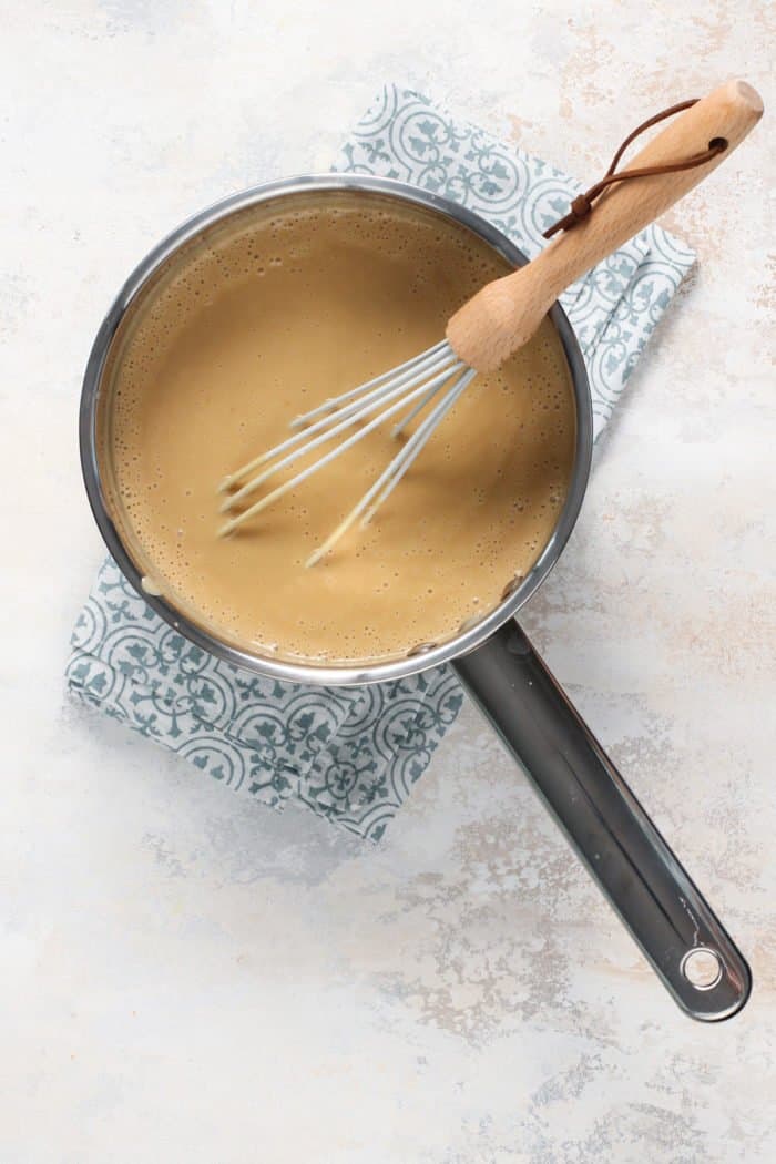 Cooked butterscotch pudding being whisked in a saucepan set on a blue tea towel.