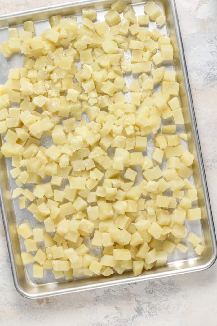 Diced potatoes cooling on a large baking sheet.