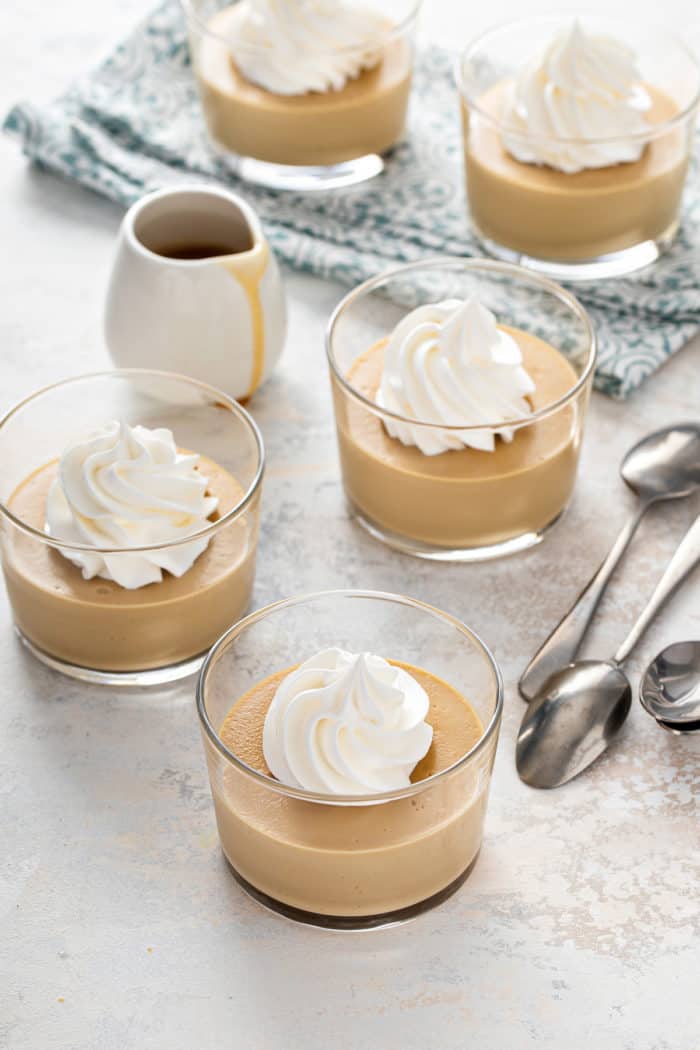 Small glass dishes filled with butterscotch pudding and topped with whipped cream scattered on a countertop.