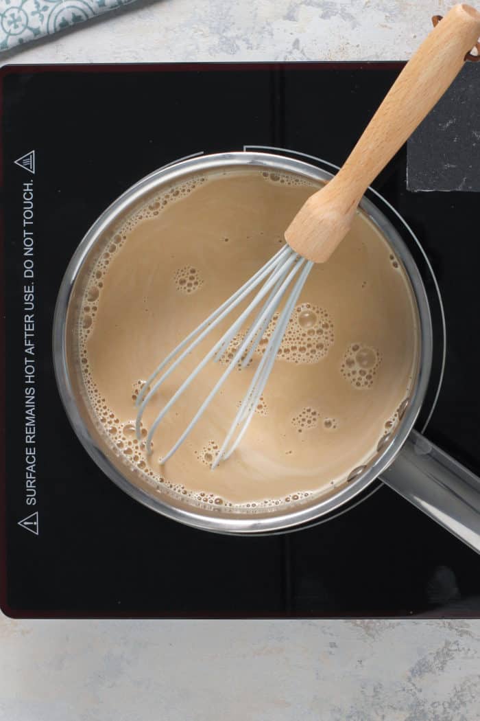 Milk and brown sugar mixture being whisked together in a saucepan on a burner.