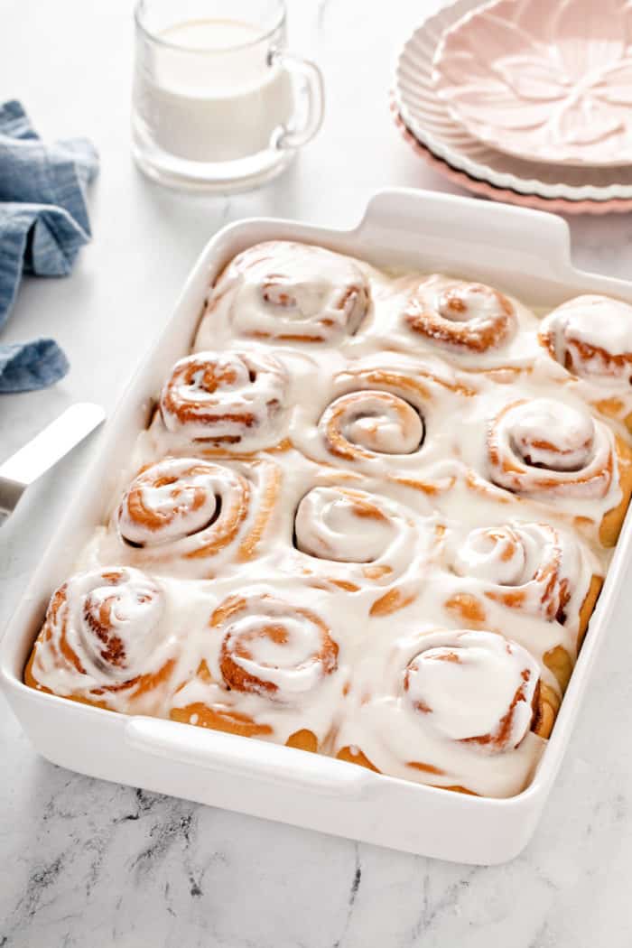 Iced overnight cinnamon rolls in a white pan