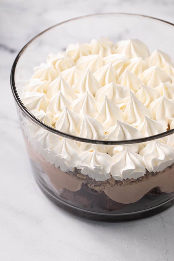 Layer of whipped topping on top of brownie and chocolate cream in a trifle dish.