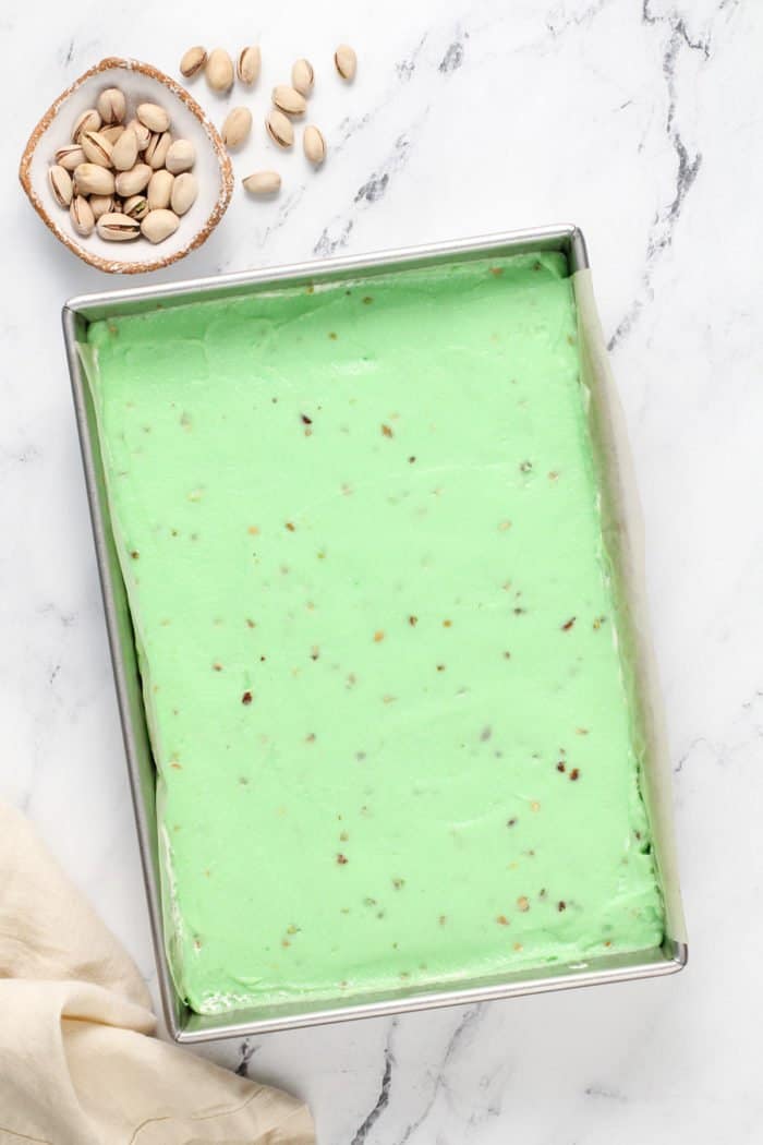 Assembling pistachio pudding dessert in a metal pan. The layer of pistachio pudding is on top in the photo.