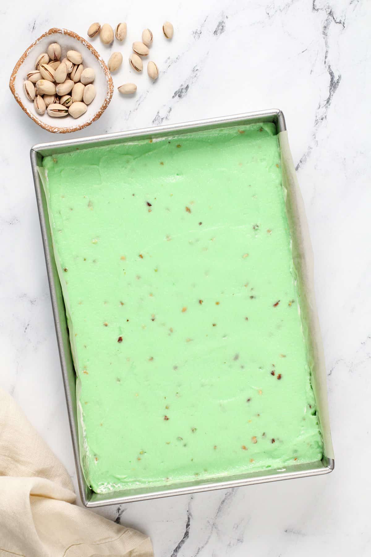 Assembling pistachio pudding dessert in a metal pan. The layer of pistachio pudding is on top in the photo.