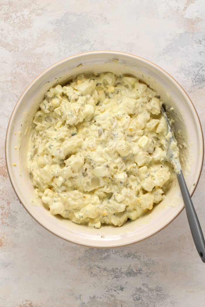 Spatula stirring together easy potato salad in a ceramic mixing bowl.