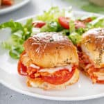 Close up image of pizza sliders on a white plate next to a green salad.