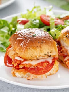 Close up image of pizza sliders on a white plate next to a green salad.