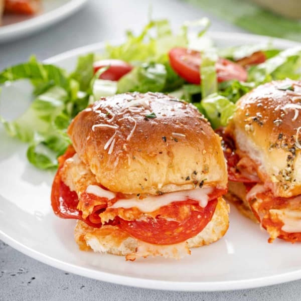 Close up image of pizza sliders on a white plate next to a green salad.