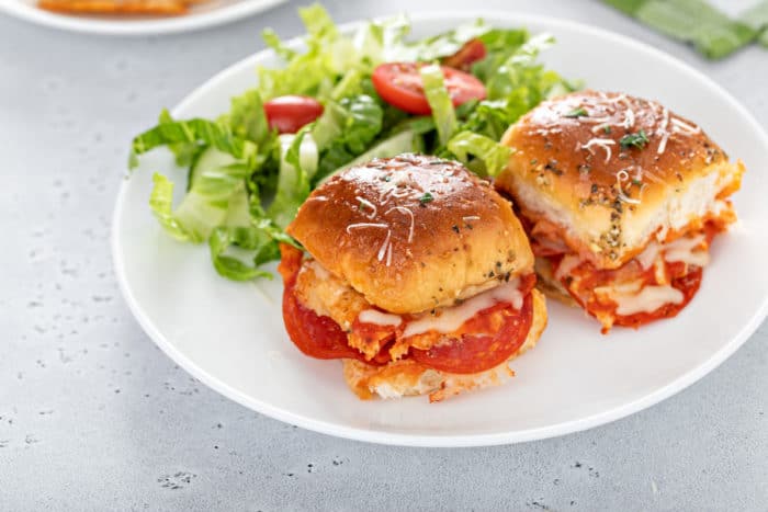 Two pepperoni pizza sliders plated next to a green salad on a white plate.