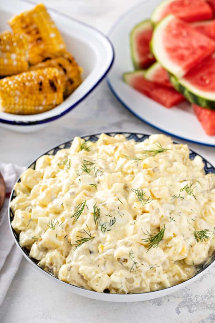 Large bowl filled with easy potato salad, with bowls of grilled corn and watermelon in the background. 