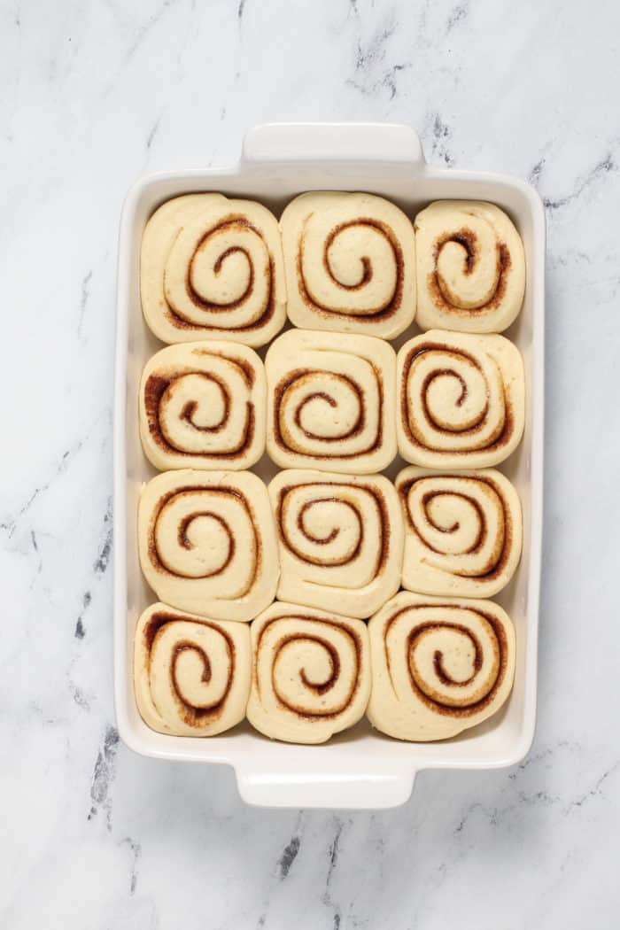 Overhead view of risen cinnamon rolls in a white pan, ready to be baked