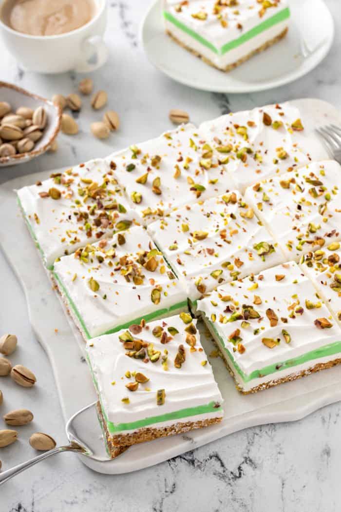 Sliced pistachio pudding dessert on a marble countertop with a piece being removed from the corner.