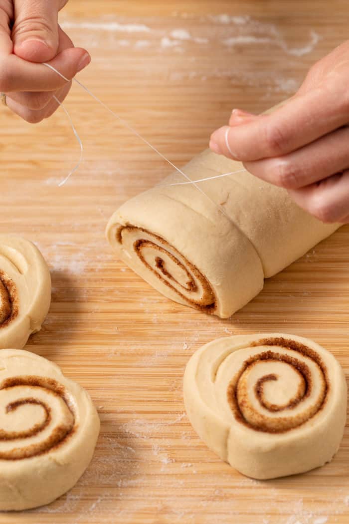 Hands using dental floss to cut cinnamon rolls