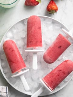 Four strawberry popsicles arranged on a bowl of ice on a marble countertop.