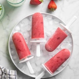 Quatre sucettes glacées aux fraises disposées sur un bol de glace sur un dessus en marbre.