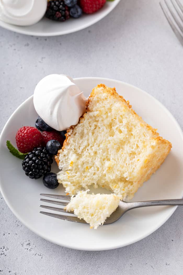 Plated slice of pineapple angel food cake with a fork taking a bite from the corner.