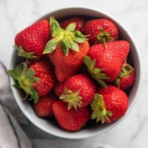 White bowl filled with fresh strawberries set on a marble countertop.