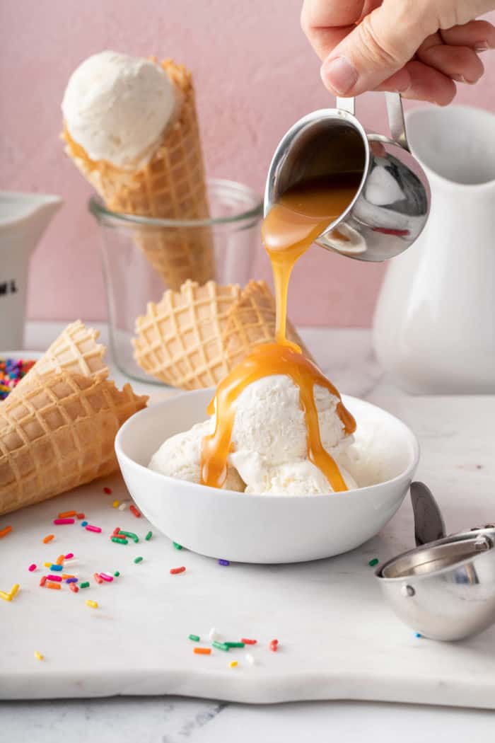 Caramel sauce being poured over no-churn ice cream in a white bowl.