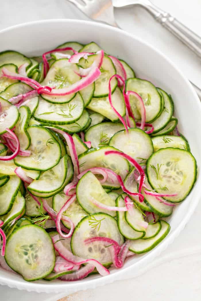 Close up of cucumber salad in a white serving bowl.