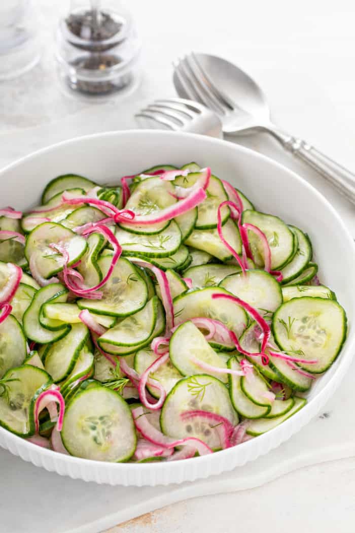 White serving bowl filled with cucumber salad on a light-colored countertop.