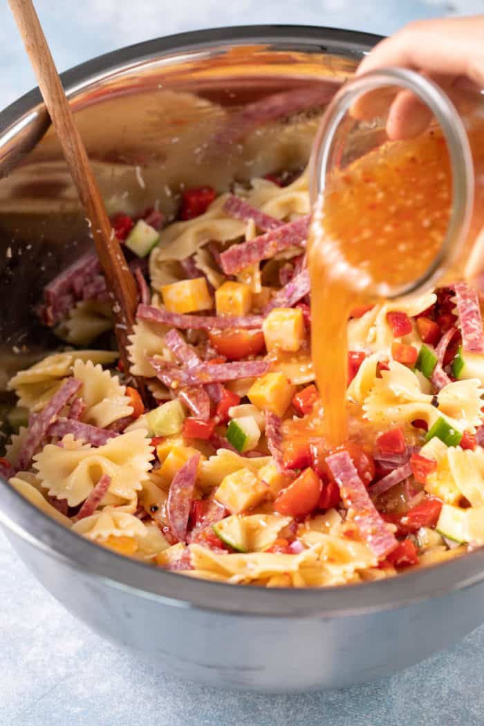 Dressing being added to italian pasta salad in a metal mixing bowl.