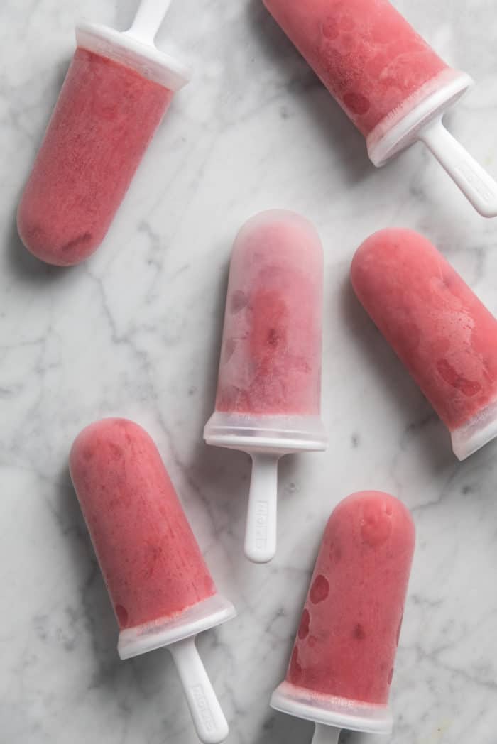 Frozen strawberry popsicles still in their molds arranged on a marble countertop.